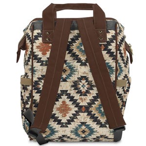 May include: Backpack with a geometric pattern in shades of brown, blue, and orange on a cream background. The backpack has brown straps, a top handle, and side pockets. The straps are adjustable and the bag appears to be made of a durable material.