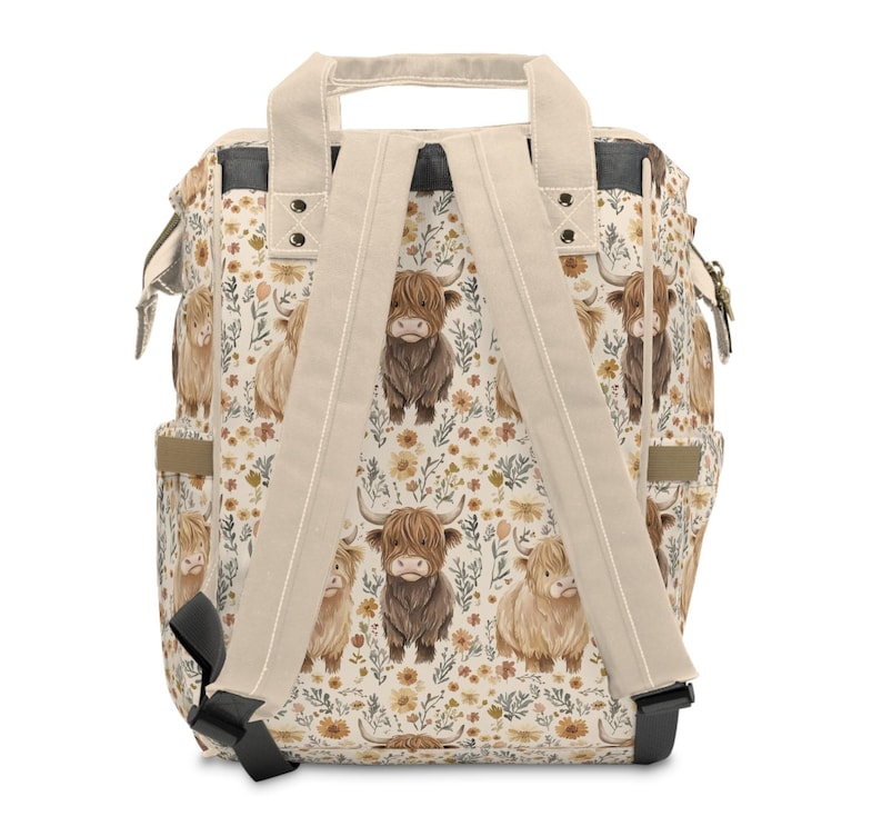 May include: A cream-colored backpack with a repeating pattern of Highland cows and floral elements in shades of brown, tan, and yellow. The backpack has beige straps and a top handle, with black accents on the bottom and sides.