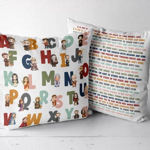 May include: Two white decorative throw pillows. One pillow features a colorful alphabet with illustrated figures. The other pillow has text about various figures. The pillows are on a white surface.