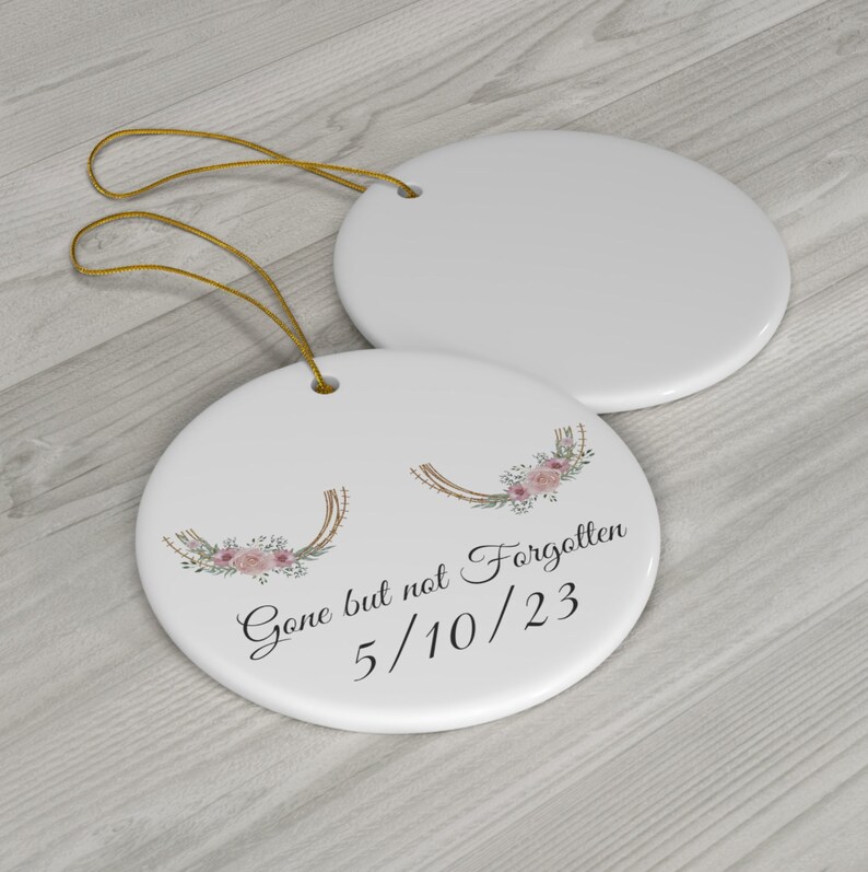 May include: White ceramic ornament with a floral wreath design and the text "Gone but not Forgotten 5/10/23".