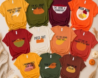 Può includere: Una collezione di magliette colorate con grafiche e testo a tema Ringraziamento. Le magliette sono in vari colori, tra cui arancione, verde e bordeaux, con frasi come "Nobody Puts Gravy in the Corner" e "I'm All About That Baste."
