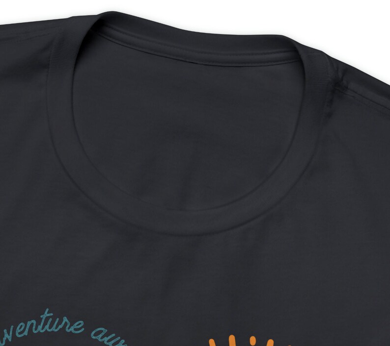 May include: Dark navy blue t-shirt with the words "adventure awaits" in teal script and a sun graphic in orange. The shirt has a crew neck and is made of a soft material.