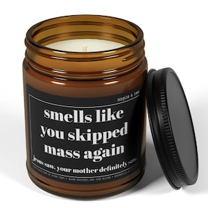 May include: A brown glass jar candle with a black lid, featuring the text "smells like you skipped mass again." The candle has a white wax interior and a label that also includes the text "Jesus saw. your mother definitely saw."