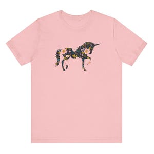 Puede incluir: Camiseta rosa claro con un dise&ntilde;o de unicornio floral. La silueta del unicornio est&aacute; llena de un patr&oacute;n de flores y hojas en tonos verdes, amarillos y rosas. La camiseta es de estilo cuello redondo cl&aacute;sico.