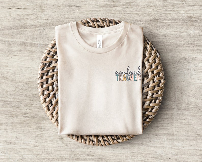 May include: A beige t-shirt with the text "second grade teacher" in colorful letters.