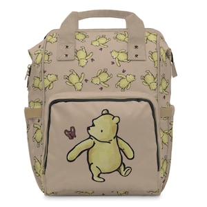 May include: A tan backpack featuring a repeating pattern of yellow cartoon bears. The front pocket showcases a larger illustration of a bear with a butterfly. The bag has a top handle, side pockets, and a black trim.