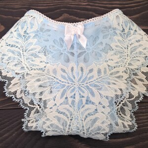 May include: Light blue underwear featuring an intricate white floral lace overlay, a scalloped edge along the waistband and leg openings, and a small white satin bow centred at the top. The text Golovenko Studio is visible on the left side.