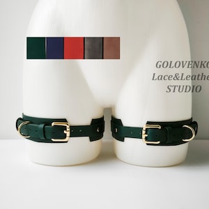 May include: A pair of dark green leather thigh straps with gold buckles and D-rings. The straps are shown on a white mannequin. The text "GOLOVENKO Lace&Leather STUDIO" is visible in the image.