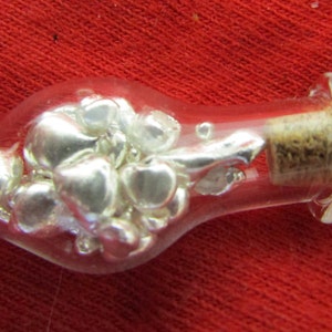 Può includere: Una piccola bottiglia di vetro con un tappo di sughero riempita di pezzi di metallo color argento.