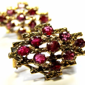 May include: A pair of gold earrings with a geometric design and red ruby stones.