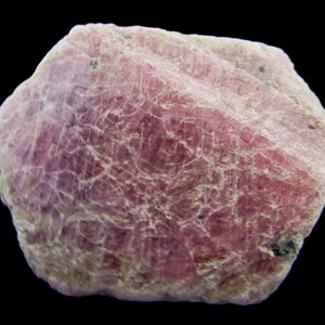Peut inclure: Un cristal de rubis rose brut avec une surface textur&eacute;e. Le cristal est opaque et a une teinte l&eacute;g&egrave;rement violette.