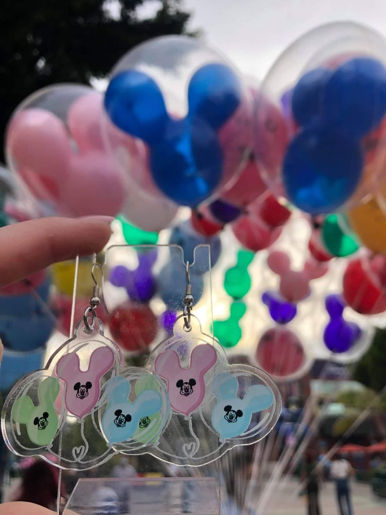 Pu&ograve; includere: Orecchini in acrilico trasparente con un design a forma di testa di Topolino. Gli orecchini presentano un gruppo di tre palloncini a forma di testa di Topolino in rosa, blu e verde.