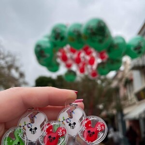 Pu&ograve; includere: Un portachiavi in plastica trasparente con tre ciondoli a forma di palloncino Mickey Mouse. I palloncini sono rossi, bianchi e verdi e presentano il viso di Mickey Mouse e fiocchi di neve. I palloncini sono decorati con luci a catena e fiocchi di neve.