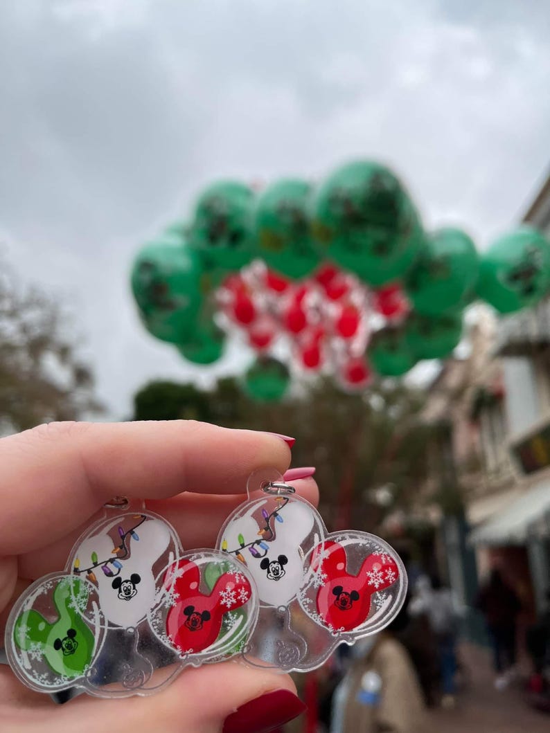 Pu&ograve; includere: Un portachiavi in plastica trasparente con tre ciondoli a forma di palloncino Mickey Mouse. I palloncini sono rossi, bianchi e verdi e presentano il viso di Mickey Mouse e fiocchi di neve. I palloncini sono decorati con luci a catena e fiocchi di neve.