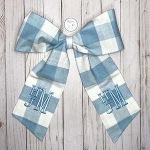 May include: A blue and white gingham bow with the monogram "HJM" embroidered on each side.