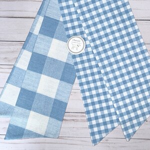 May include: Two pieces of blue and white gingham fabric. The fabric on the left has larger squares than the fabric on the right. The fabric on the right has a label that says "classic".