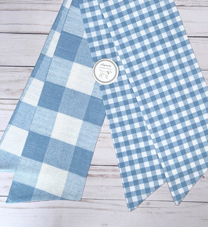 May include: Two pieces of blue and white gingham fabric. The fabric on the left has larger squares than the fabric on the right. The fabric on the right has a label that says "classic".