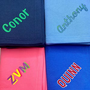 Puede incluir: Cuatro mantas personalizadas en diferentes colores con nombres bordados. Los nombres son Conor, Anthony, ZVM y Quinn.