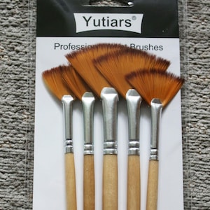 Può includere: Un set di sei pennelli a ventaglio. I pennelli hanno manici in legno marrone chiaro, ghiera in metallo argentato e setole marrone chiaro. La confezione riporta "Yutiars" e "Professional Paint Brushes".
