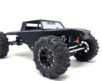 May include: Black remote control truck with large, textured tires. The truck has a cab with the word "POSER" on the windshield. The vehicle is designed for off-road use and features a detailed chassis.