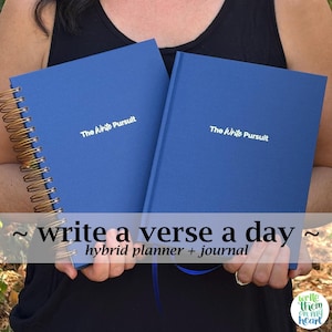 May include: Two blue journals with the text "The Write Pursuit" in white. One journal has a gold spiral binding, and the other has a solid spine. The image also includes the text "write a verse a day hybrid planner + journal".