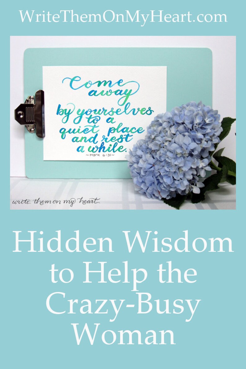 May include: A light blue clipboard holds a white card with handwritten calligraphy in teal and green, reading "Come away by yourselves to a quiet place and rest a while." A bouquet of blue hydrangeas rests beside it. The image also includes the text "Hidden Wisdom to Help the Crazy-Busy Woman."