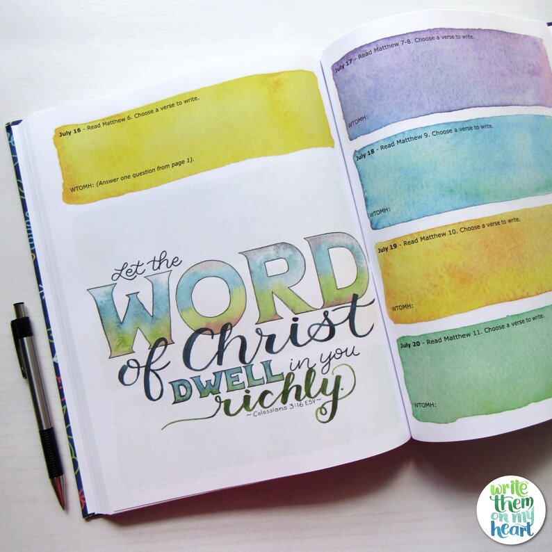 May include: Open journal with colorful watercolor accents and the text "Let the WORD of Christ DWELL in you richly." Includes prompts for writing verses from Matthew. A black pen rests on the open pages. The journal is from "Write them on my heart."