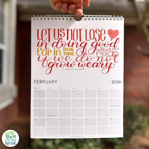 May include: A spiral-bound calendar for February 2026, held by a hand. The calendar features a handwritten quote in red and orange, with a heart graphic. The calendar also includes the text "Write Them On My Heart."