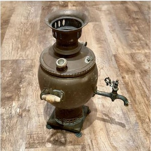 Peut inclure: Samovar en bronze antique, avec un corps rond, un robinet et un dessus décoratif. Le samovar a une poignée avec une prise de couleur claire et repose sur une base carrée. Un objet classique pour préparer le thé, environ 40 cm de haut.