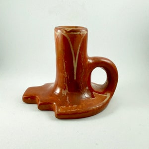 Puede incluir: Un portavelas de terracota con un diseño blanco. El portavelas tiene un asa y una base ancha.