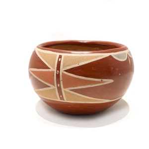 Może przedstawiać: Brązowa ceramiczna miska z geometrycznym wzorem w odcieniach beżowego i pomarańczowego. Miska ma zaokrąglony kształt i gładkie, polerowane wykończenie.