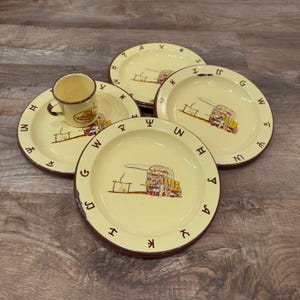 May include: A set of three cream-colored enamel plates and one matching mug, each featuring a brown rim and a central illustration of a covered wagon with a campfire. The rims are decorated with various brown western-style cattle brand symbols.
