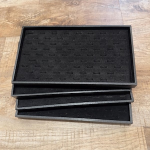 May include: A stack of three black ring display trays. Each tray has a rectangular shape with a dark gray frame and a black, felt-like interior with multiple ring slots. The trays are stacked on top of each other.