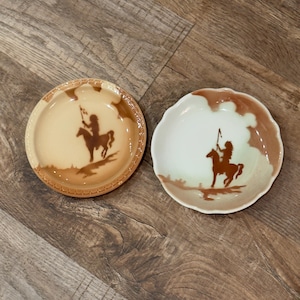 May include: Two round ceramic dishes featuring brown silhouettes of a person riding a horse and holding a spear. The left dish has a textured rim and tan glaze, while the right dish has a scalloped edge and a lighter, off-white center finish.