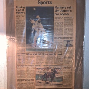 May include: A newspaper clipping with the headline "Sports" and articles about the Masters golf tournament, the Seattle Mariners baseball team, the Edmonton Oilers hockey team, and the Kentucky Derby. The image includes a photo of a baseball player pitching and a photo of a horse racing.
