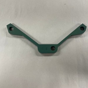 May include: A dark green metal bracket with two holes on each end and one hole in the center. The bracket has the text "F 6" stamped on it.