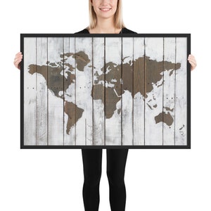 May include: A framed wood print of a world map with a whitewashed wood background. The map is in a brown color and the wood grain is visible.