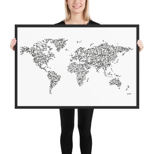 May include: A black and white world map print with a scribbled line art style. The map is framed in a black frame and is being held by a person.