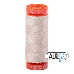 May include: A spool of light beige sewing thread with bright orange plastic ends. The top end features the embossed text AURIFIL, and the bottom end displays the text 100% COTTON. The thread is wound tightly around the central cylindrical core.