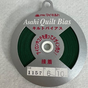 May include: A spool of green bias tape for quilting, labeled "Asahi Quilt Bias" with the Japanese characters for "Asahi" and "Quilt". The label also says "Quilt Bias" and "1157 6mm/m 10m".