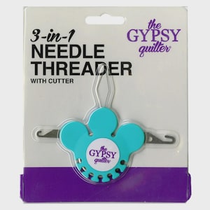 May include: A 3-in-1 needle threader with cutter, packaged on a white and purple card. The threader is turquoise and shaped like a flower, with the text "the GYPSY quilter" on the front. The packaging reads "3-in-1 NEEDLE THREADER WITH CUTTER".