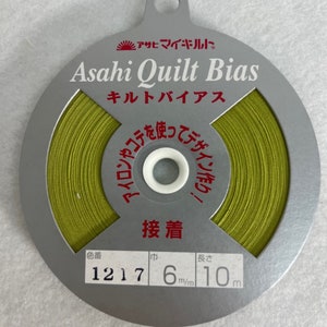 May include: A spool of green bias tape for quilting. The label reads "Asahi Quilt Bias" and includes the text "キルトバイアス" in Japanese. The label also indicates the color number is 1217, the width is 6 mm, and the length is 10 meters.