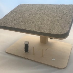 May include: A wooden sewing stand with a gray felt-covered top. The stand has a small spool holder, a needle holder, and a pin cushion.