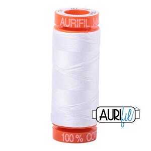 May include: A spool of white sewing thread with orange plastic ends. The top end features the text AURIFIL and the bottom end features the text 100% COTTON. The thread is wound around a cylindrical core, and the Aurifil logo is visible in the corner.