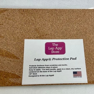 May include: A brown cork protective pad with self-stick adhesive. The pad is designed to fit the Lap App and protect surfaces from scratches and marks. The pad is 1/8 inch thick. The text "The Lap App Store" and "Lap App® Protective Pad" is printed on a white label.