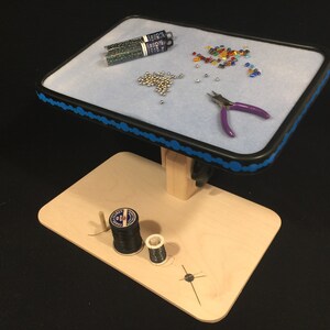 May include: A wooden beading and crafting workstation with a light blue felt surface, black trim, and blue decorative accents. It holds beads, tools, and spools of thread. The workstation is designed for jewelry making and other crafts.