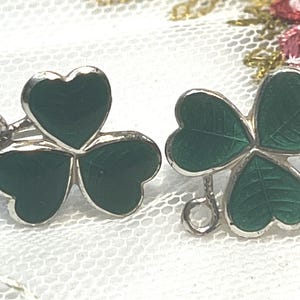 May include: Two silver shamrock charms with green enamel. Each charm has a loop for attaching to a necklace or bracelet.