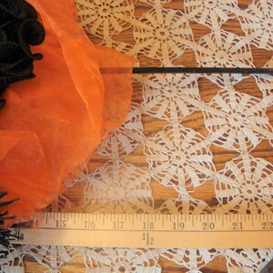 May include: A Halloween-themed image featuring a black and orange witch's broom with a black handle. The broom is adorned with black ribbon and orange fabric. A ruler is placed near the broom, measuring approximately 23 inches.