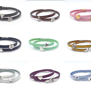 Op de afbeelding: Tien verschillende lederen armbandjes met verschillende bedels, waaronder een blad, een ster, een anker, een veer, een hart, een oneindigheidssymbool, een slang, een bloem, een golfbal en een diamant.
