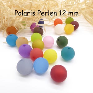 Könnte beinhalten: Eine Ansammlung farbenfroher Polaris Perlen-Perlen mit einem Durchmesser von 12 mm in verschiedenen Farbtönen wie Blau, Gelb, Rosa und Rot. Die Perlen liegen auf einer weißen Oberfläche mit Dekostroh.
